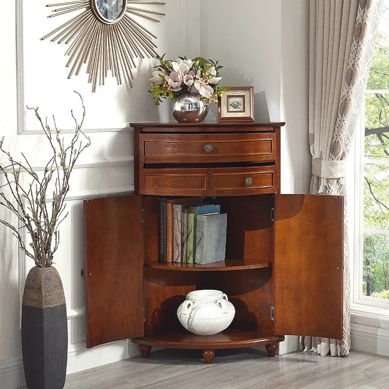 Wooden corner cabinet with open doors displaying books and decor items, next to a vase with flowers and a mirror.