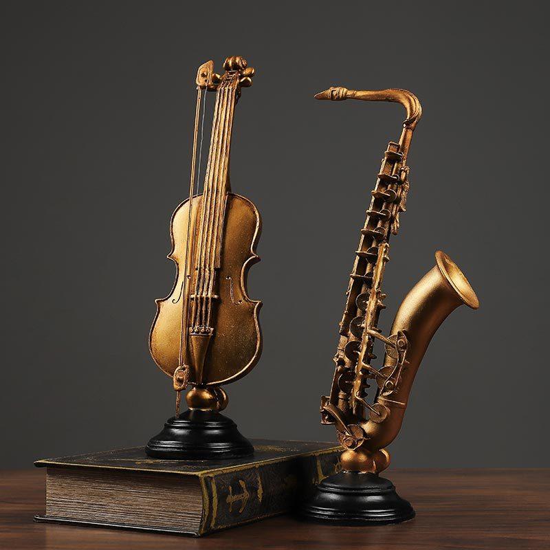 A model of a violin and a saxophone made from resin, crafted in a vintage style, displayed on a wooden surface.