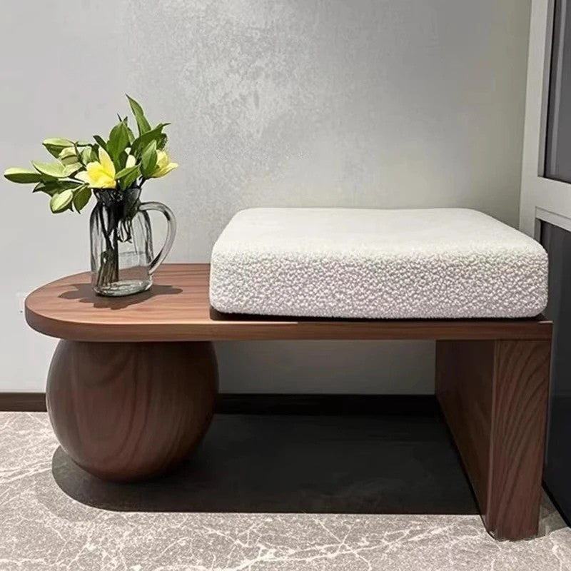 Wooden side table with a white cushion and a vase of flowers against a neutral wall.