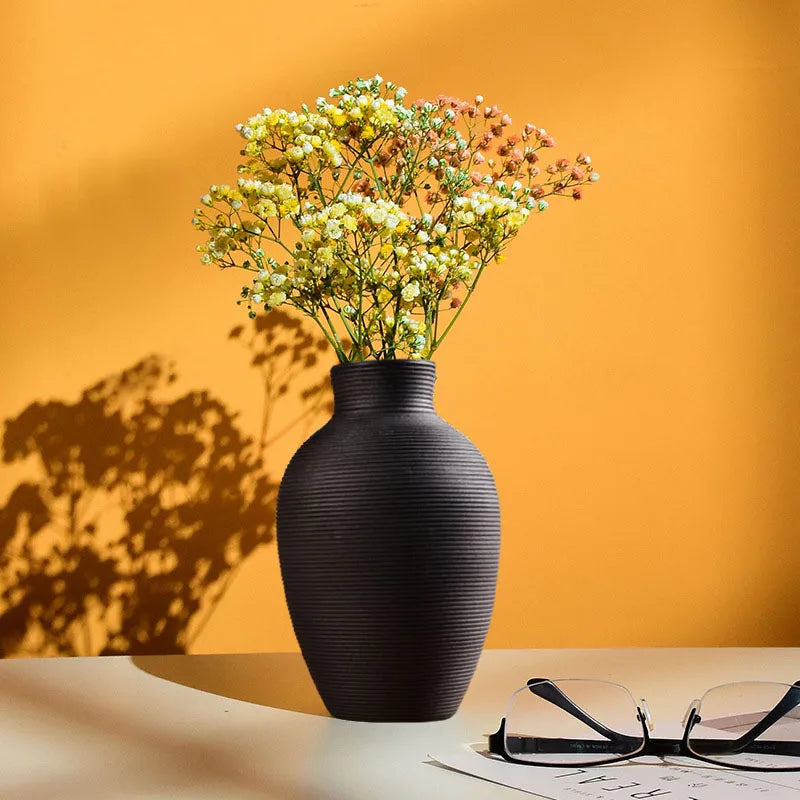 Black vase with dried flowers on a table against an orange wall