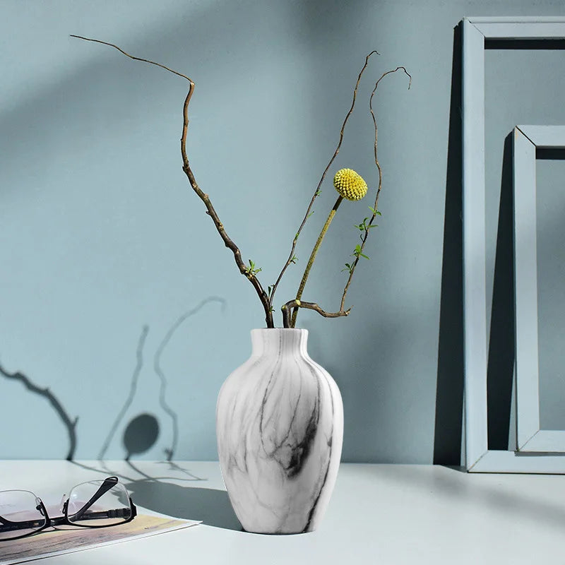 White marble-patterned vase with branches and a yellow flower against a light blue wall.