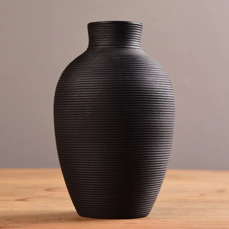 Black ribbed vase on a wooden surface with a neutral background