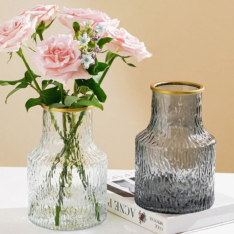 Two glass vases with one containing pink flowers on a light surface with a beige background
