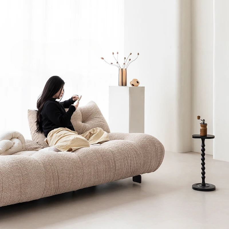 Person sitting on a modern beige sofa in a minimalistic room with a small table and decorative items.