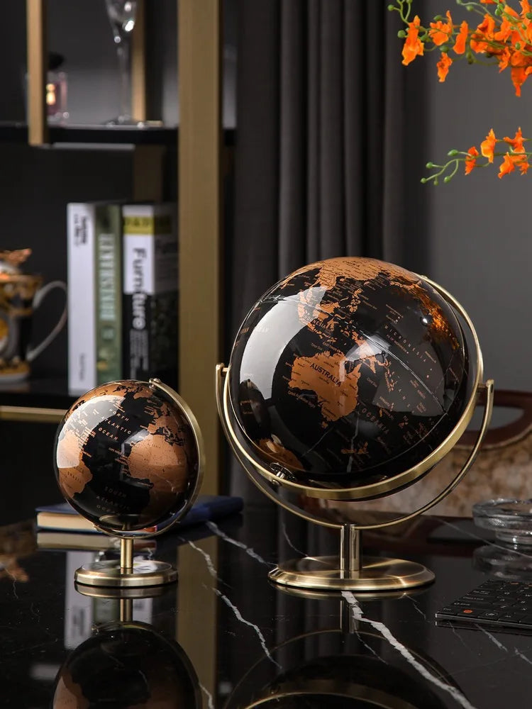 Two decorative globes on a reflective surface with books and a plant in the background.