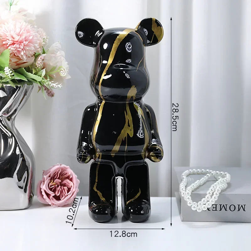 Black and gold bear-like figurine with measurements on a white surface with flowers and jewelry.