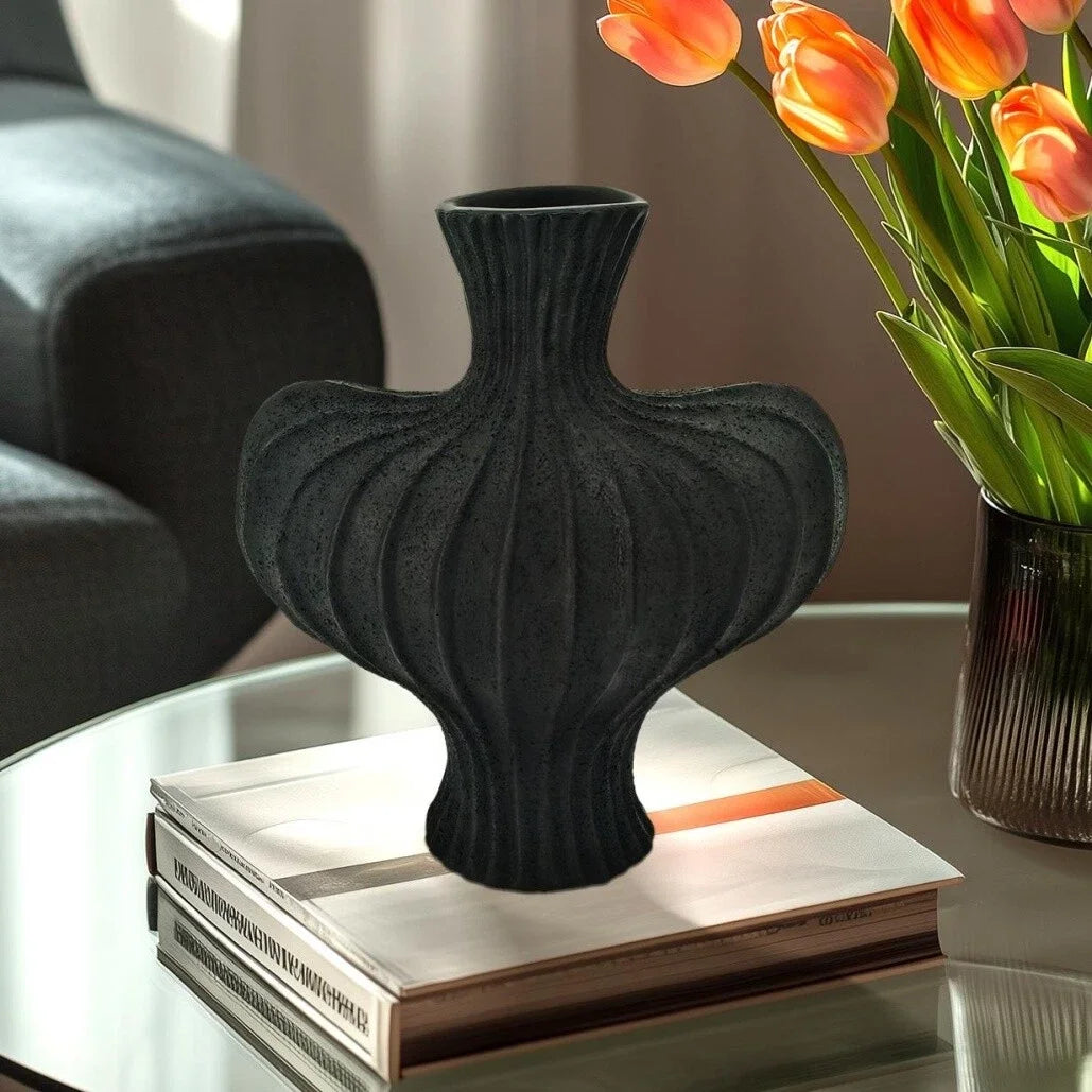 Black textured vase on a stack of books with a vase of tulips in the background