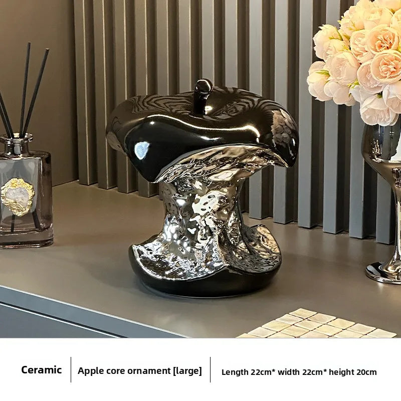 Decorative ceramic apple core ornament on a surface with a vase and diffuser in the background.