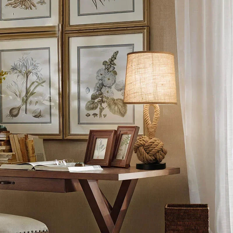 Decorative lamp on a wooden table with framed botanical prints on the wall.