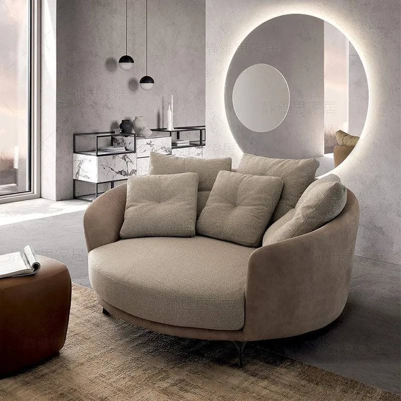 Modern living room with a curved beige sofa, round mirror, and minimal decor.