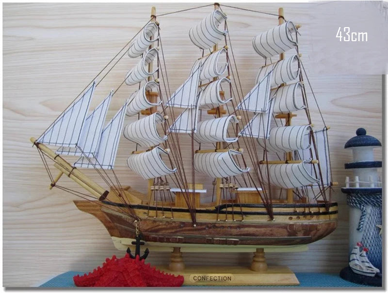 Wooden model ship with multiple sails on a wooden base, against a light wood panel background.