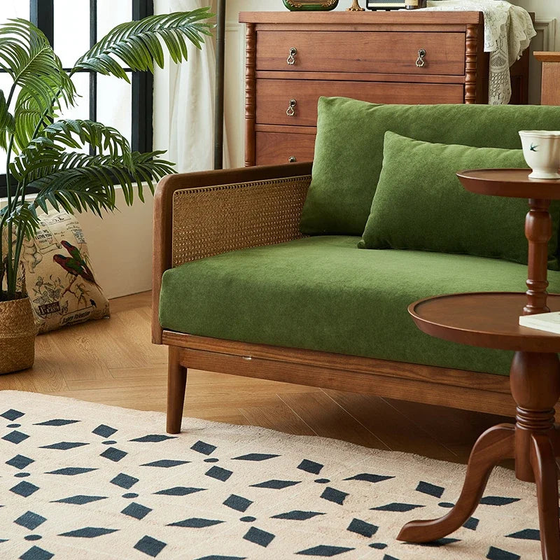 Green sofa with wooden frame in a room with a plant and side table.