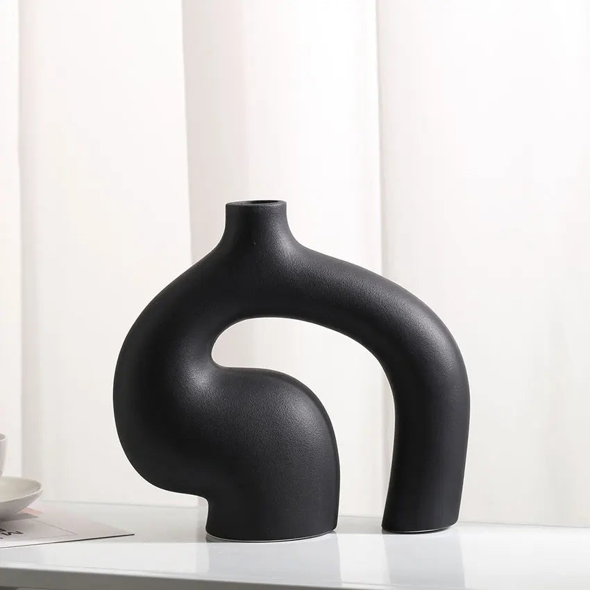 Black abstract vase on a white surface with a white curtain background