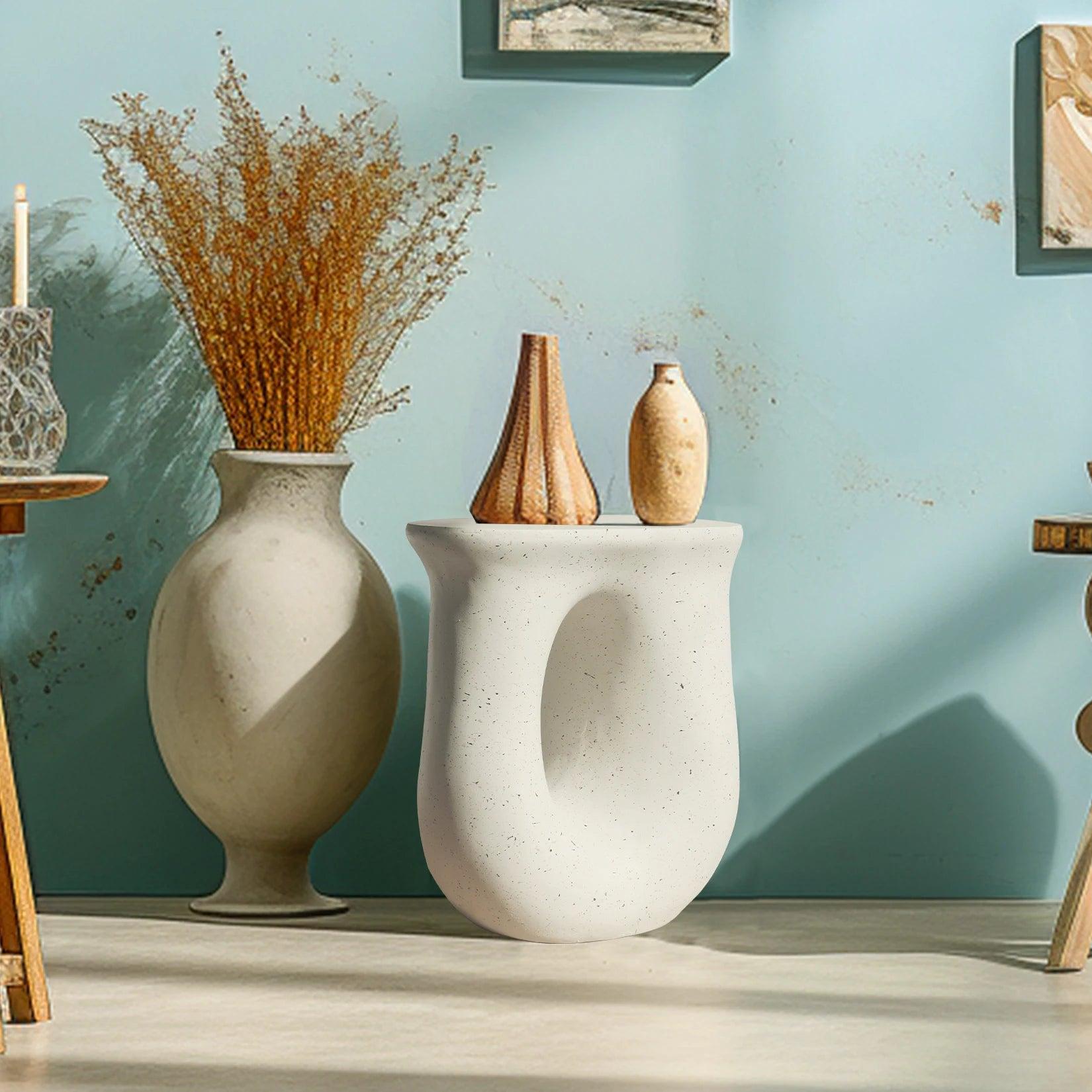 A modern indoor and outdoor side table featuring a U-shaped design with a light off-white concrete construction, displayed in a home setting with decorative items on top.