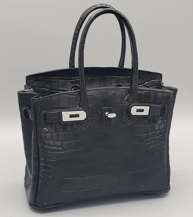 Black crocodile-patterned handbag with silver hardware on a light Grey background  Modern white tabletop flower holder