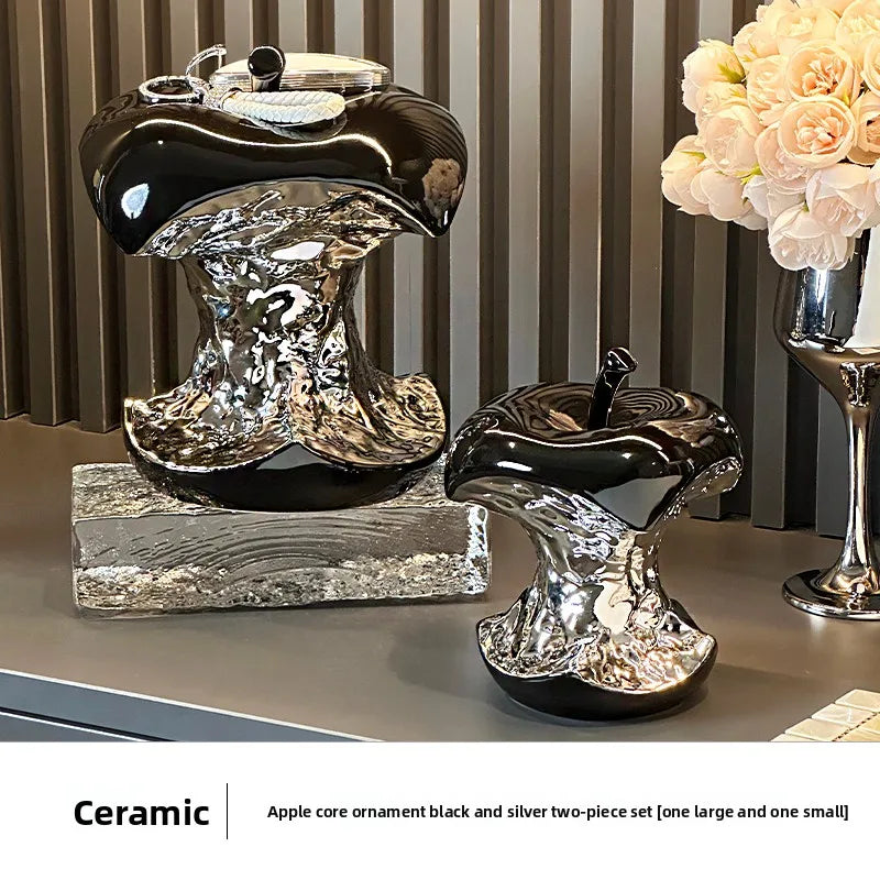 Ceramic apple core ornaments in black and silver on a surface with a striped wall in the background.