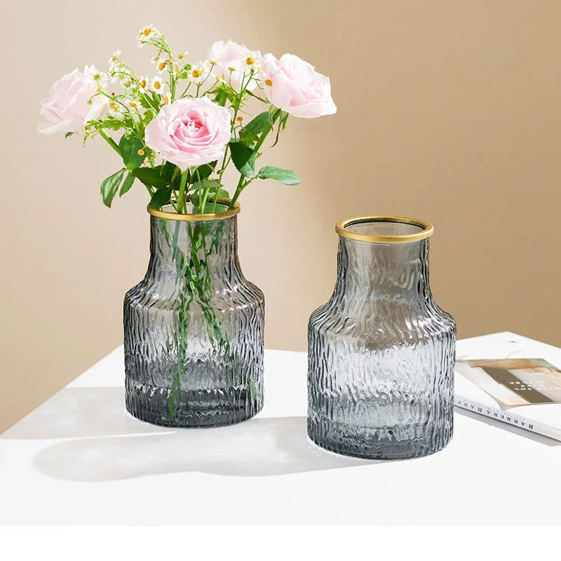 Two gray glass vases with gold rims on a white surface against a beige background