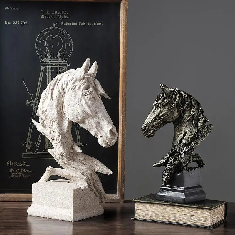 Two horse head sculptures, one white and one bronze, on a wooden surface with a framed patent drawing in the background.