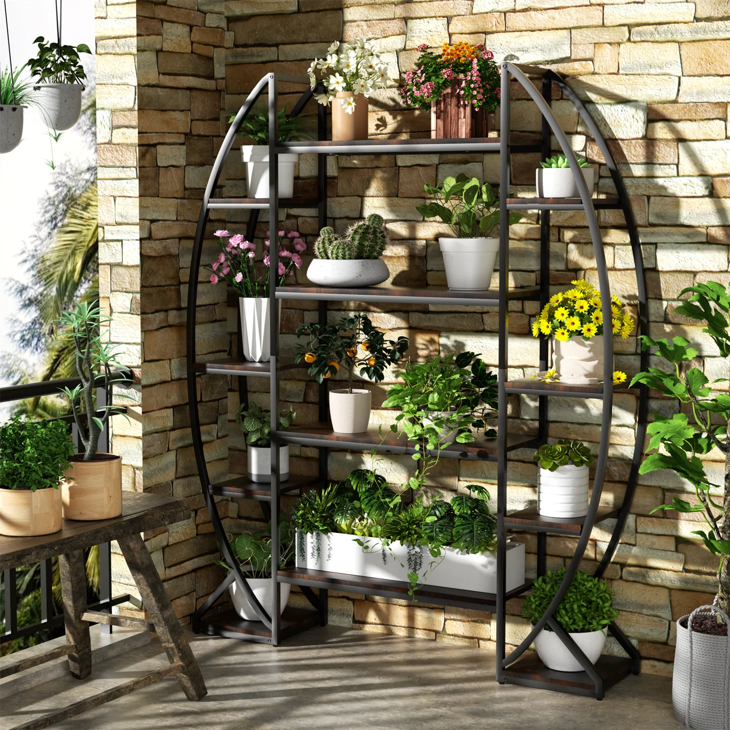 A large half-moon industrial plant stand made of iron and MDF, displaying a variety of potted plants across its five tiers, placed in a home setting with brick wall and patio furniture.