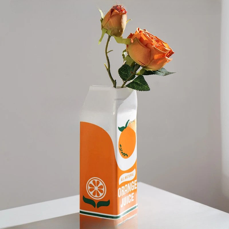 Orange juice carton repurposed as a vase with orange roses on a gray background