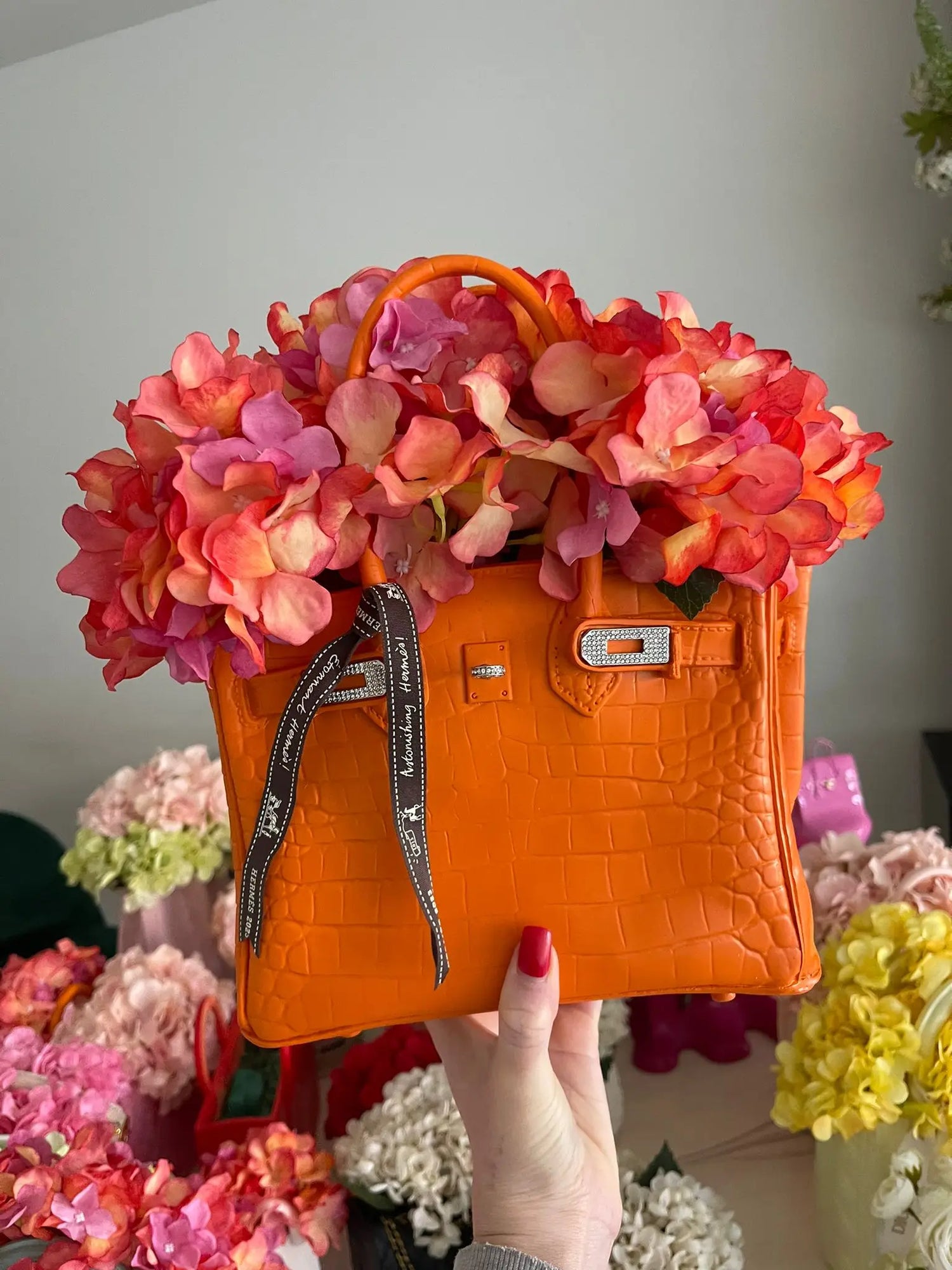 Orange handbag with floral design held by a hand against a floral Modern aesthetic resin vase background