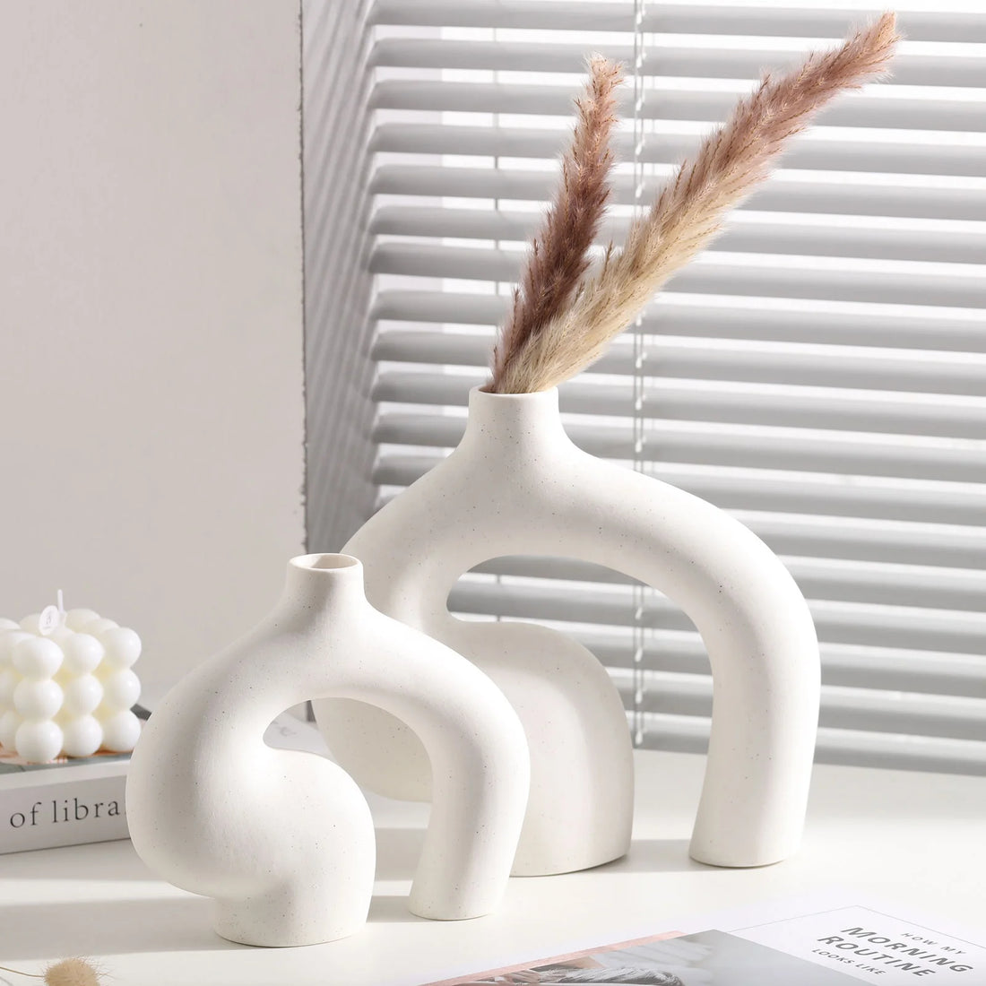 Set of three white ceramic vases with dried pampas grass against a neutral background