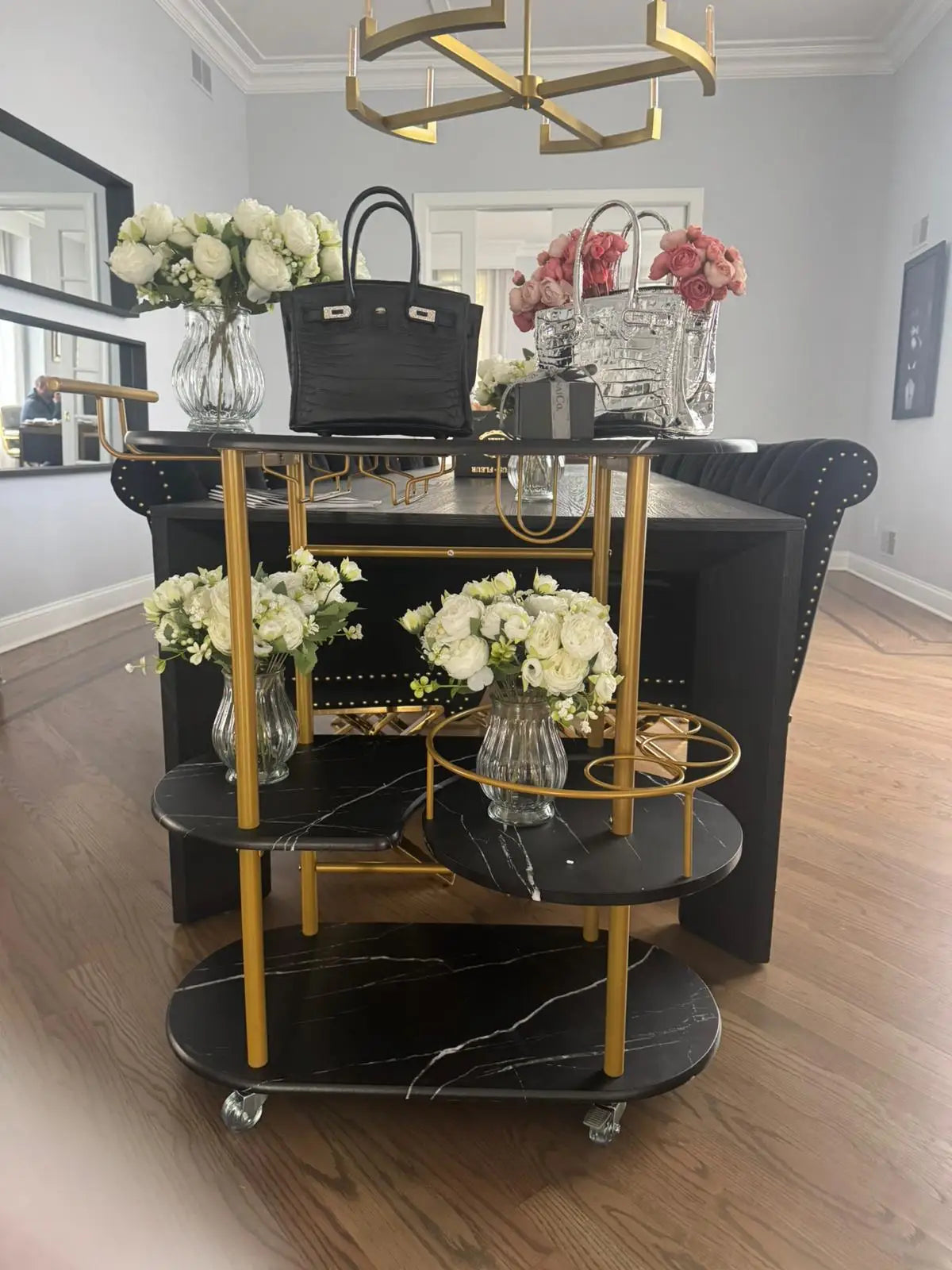 Black and gold serving cart with flowers and bags in a room. Stylish wedding table flower vase
