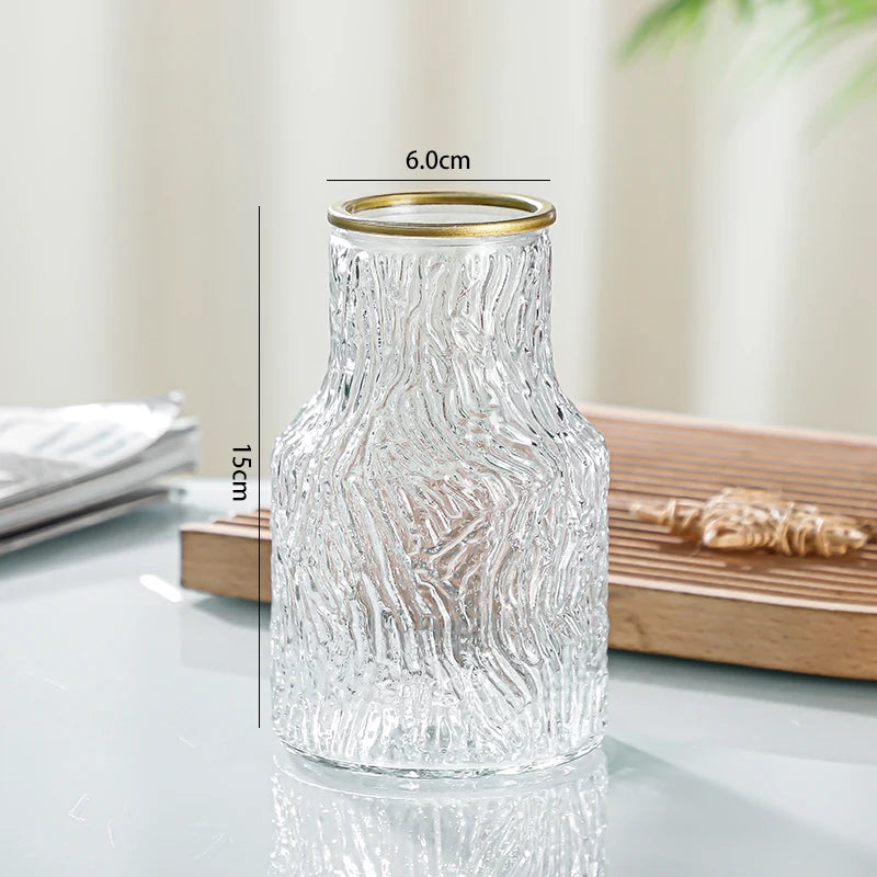 Clear glass vase with gold rim on a reflective surface, with measurements indicated.