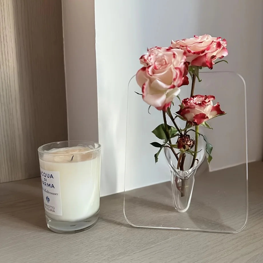 Clear glass vase with pink roses and a candle on a wooden surface.