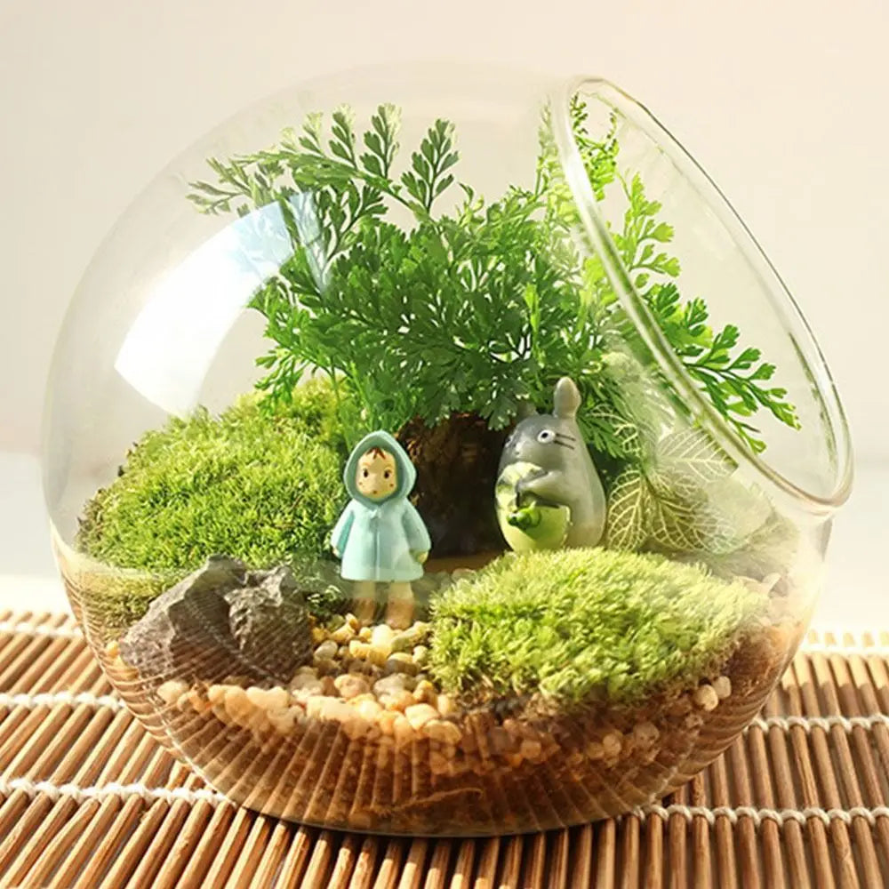 Terrarium with plants, small figures, and pebbles on a woven surface