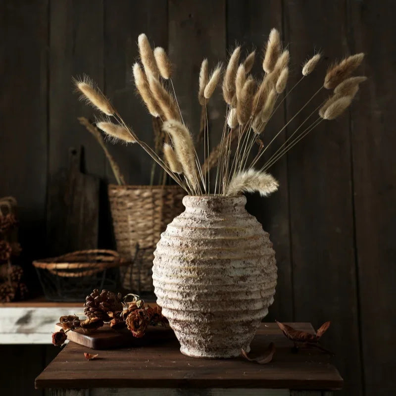 Decorative vase with dried plants on a wooden surface against a dark wooden wall.