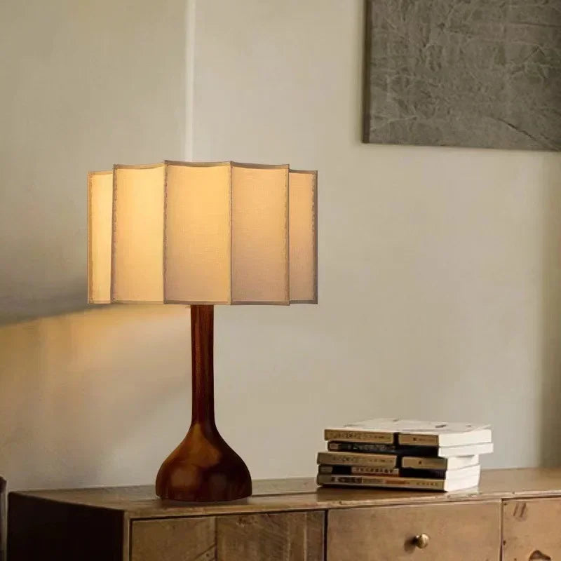 Table lamp with a wooden base and beige fabric shade on a wooden surface.