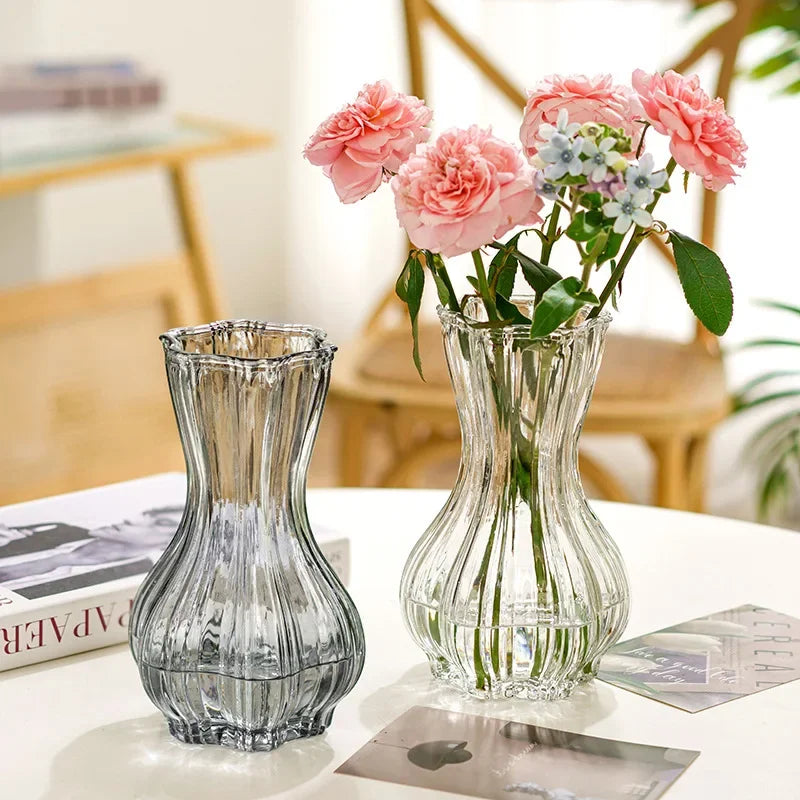 Two glass vases with flowers on a table in a home setting