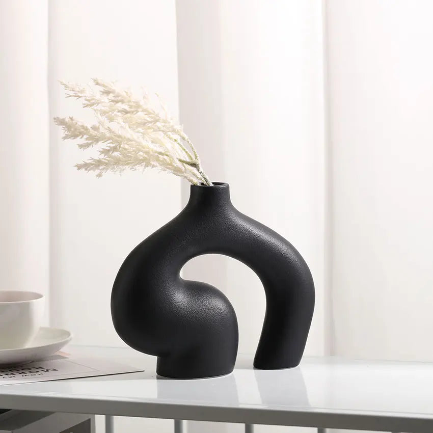 Black vase with dried plants on a white surface with a light background