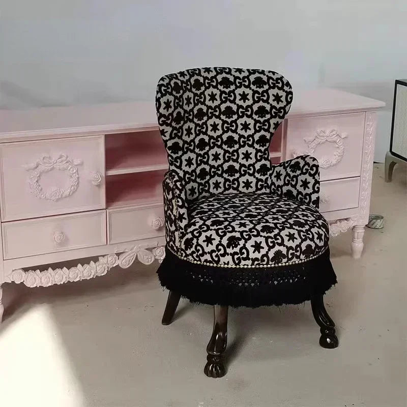 Decorative chair with black and white pattern in front of a pink dresser.