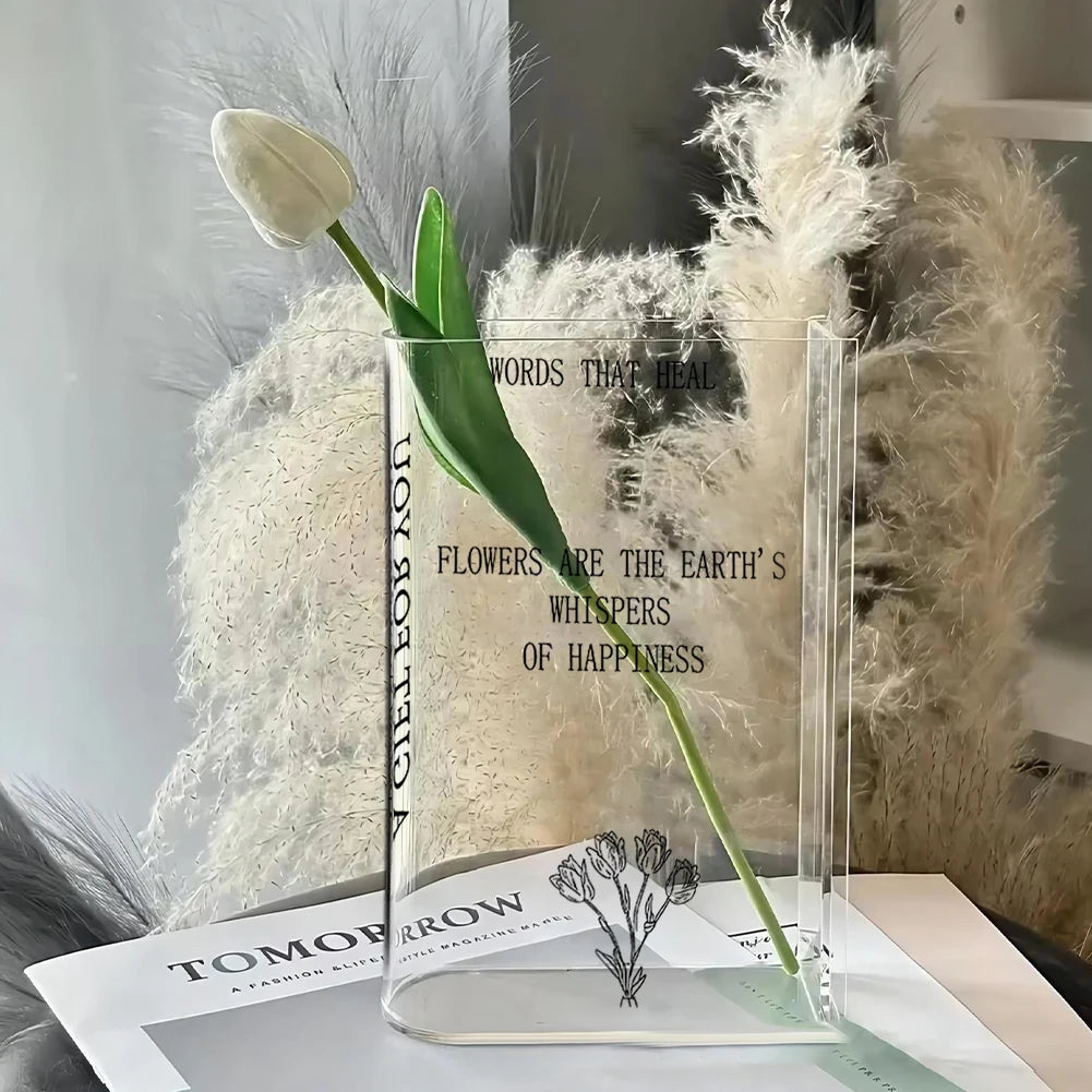 Clear acrylic stand with a tulip and decorative text, placed on a surface with a blurred background.