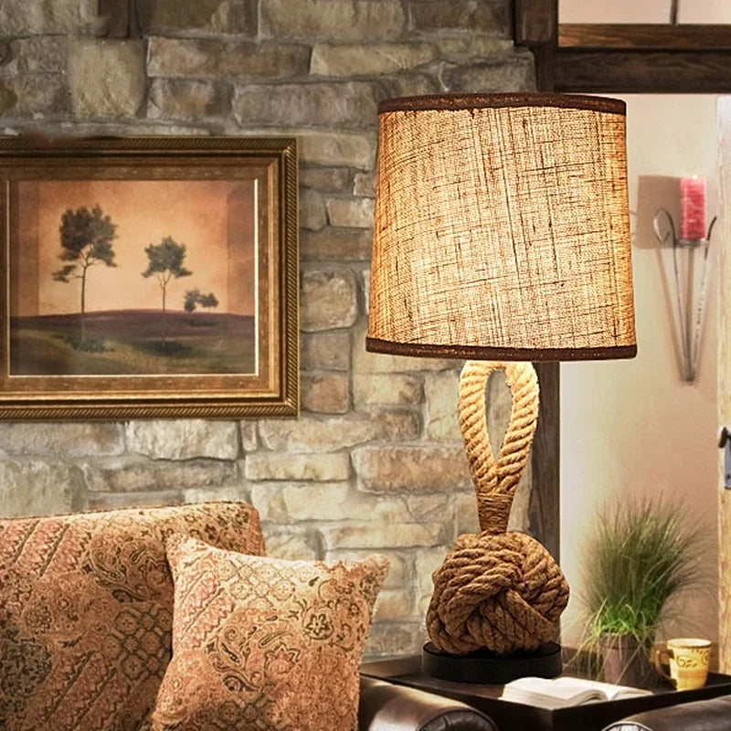Rustic lamp with knotted base on a table against a stone wall with a painting.