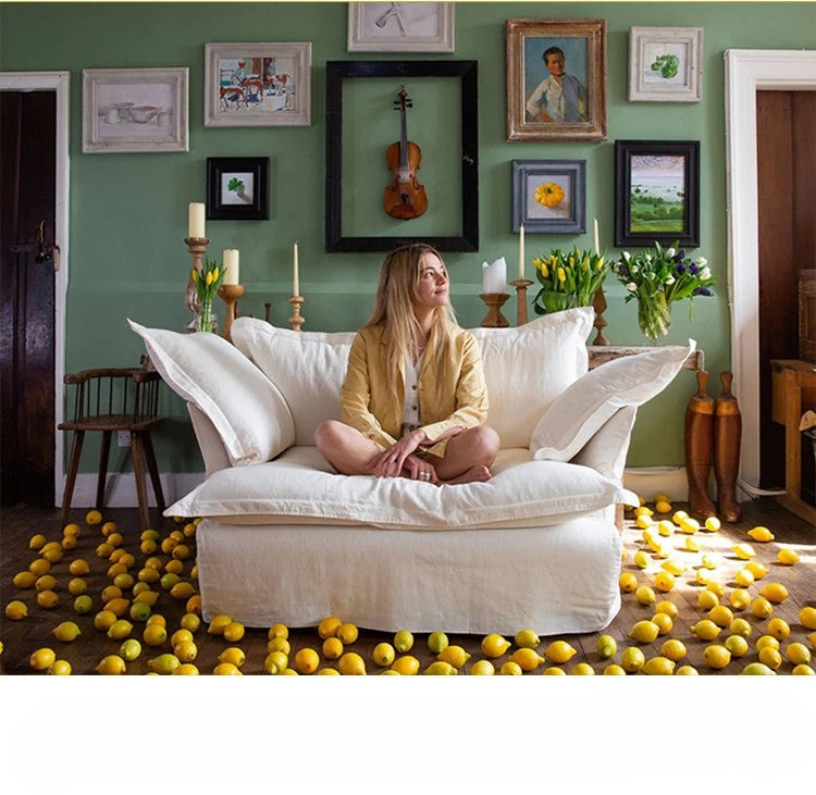 Woman sitting on a white sofa with lemons scattered around in a room with green walls and framed pictures.