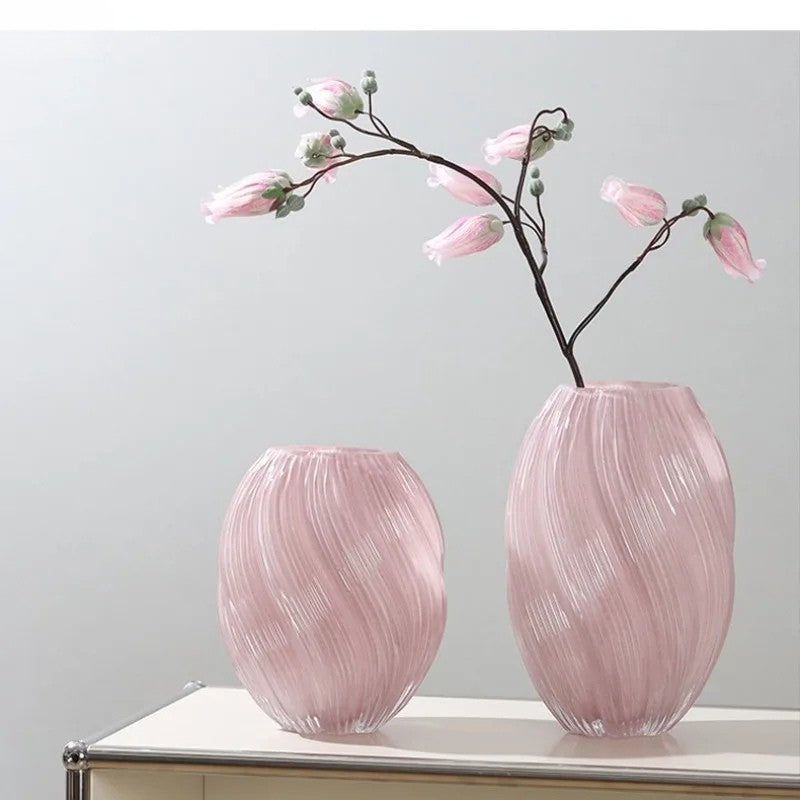 Two pink glass vases with floral branches on a light surface against a light gray background