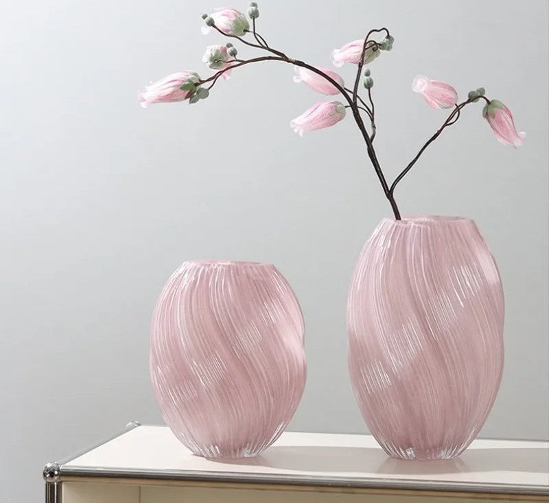 Two pink glass vases with floral branches on a light surface against a light gray background