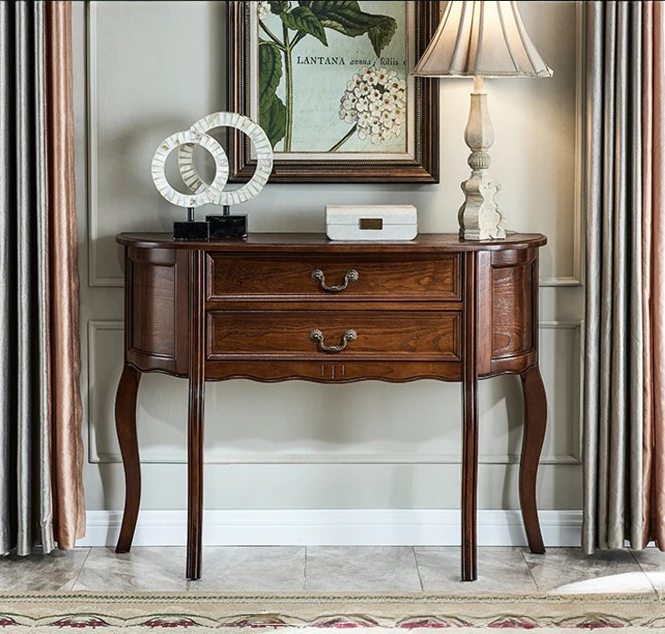 Wooden console table with decorative items in a room with curtains and a lamp.