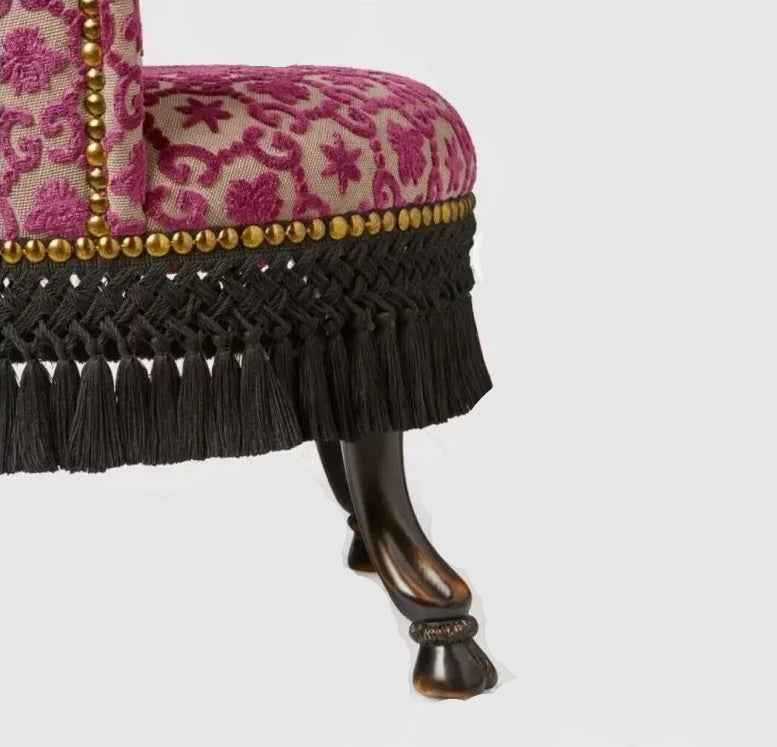 Close-up of a decorative chair with pink floral pattern and black fringe on a white background