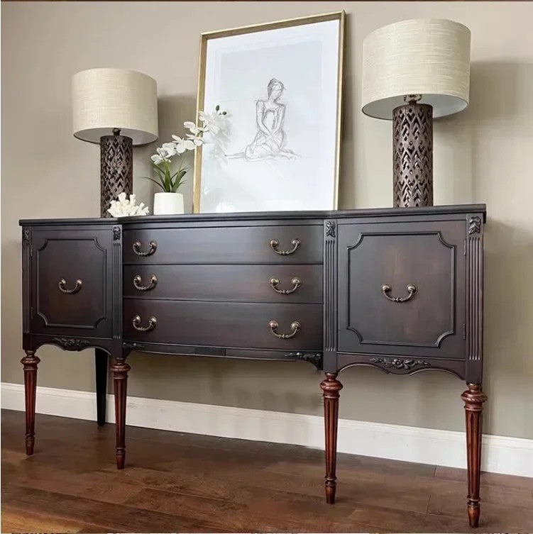 Dark wooden sideboard with two lamps and a framed picture on a wall.