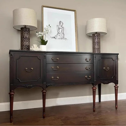 Dark wooden dresser with two lamps and a framed picture on a beige wall.