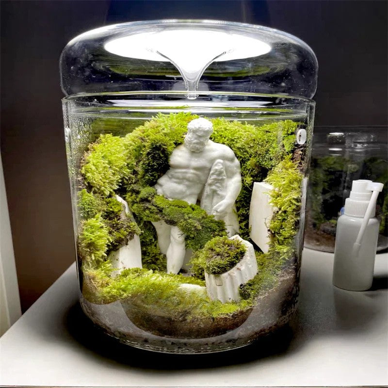 Terrarium with a statue and greenery inside a glass container on a table.