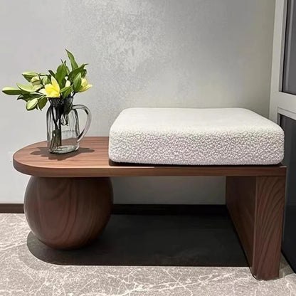 Wooden side table with a white cushion and a vase of flowers against a neutral wall.