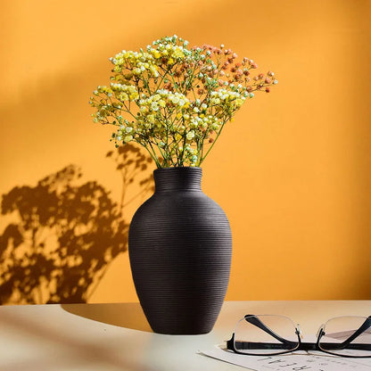 Black vase with dried flowers on a table against an orange wall