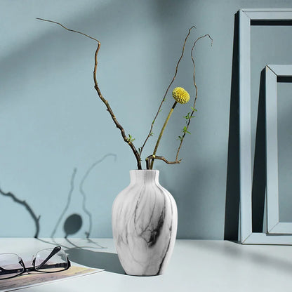 White marble-patterned vase with branches and a yellow flower against a light blue wall.