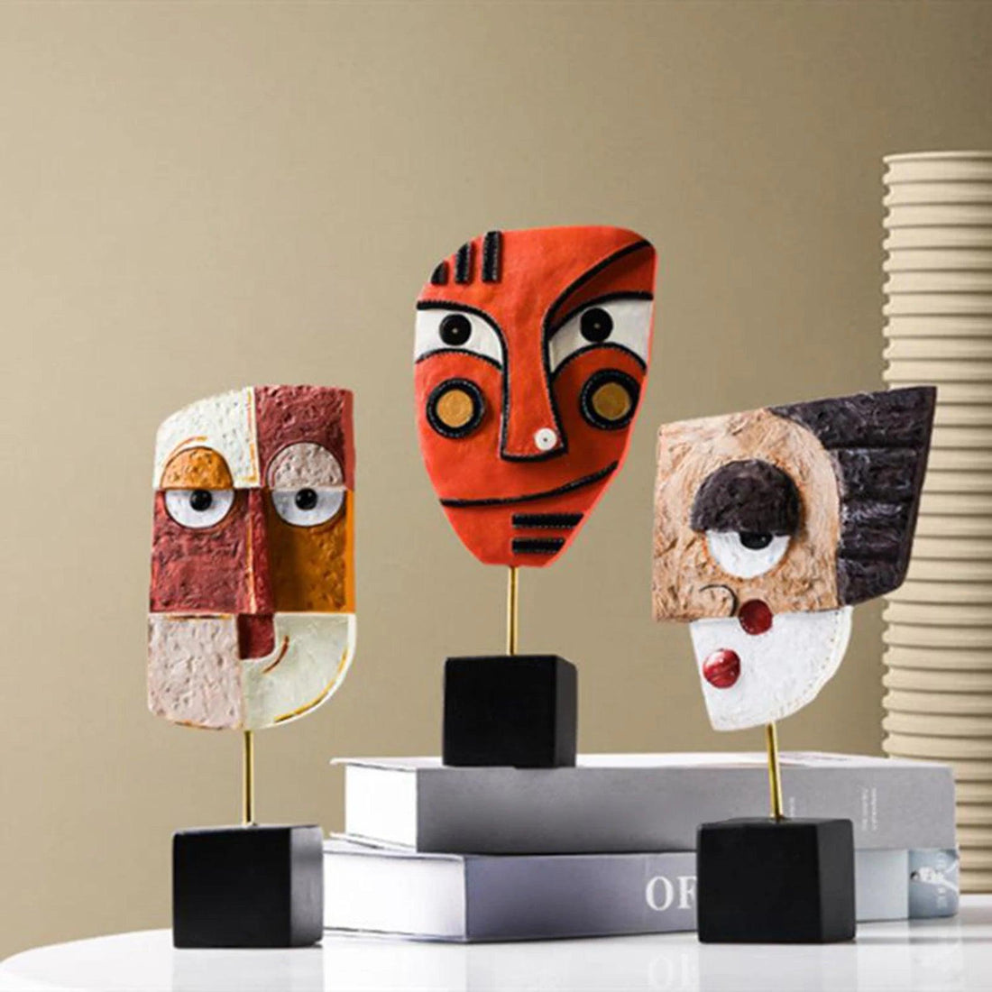 Three abstract resin figurines in different colors representing creative face art, displayed on black stands, positioned on top of a white surface with a neutral background.