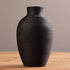 Black ribbed vase on a wooden surface with a neutral background